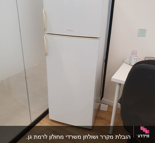 מקרר לבן עומד ליד שולחן וכיסא